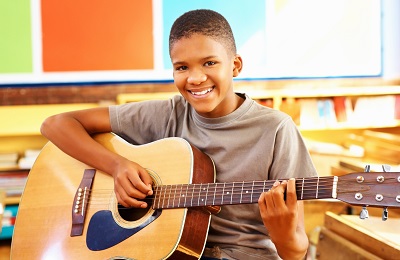 child with a smile holding a
			guitar